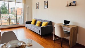 Een moderne woonkamer met een grijze bank, gele kussens, een houten bureau met een laptop en een eettafel gedekt met borden en glazen.