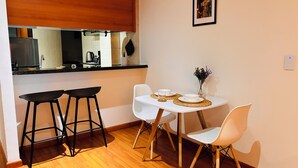 Een gezellige keuken met een houten aanrecht, twee barkrukken, een eettafel met witte stoelen en een kleine potplant.