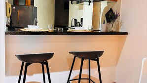 Een moderne keuken met een houten aanrecht, twee zwarte barkrukken en een witte stoel.