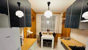 A compact kitchen with white cabinets, a wooden countertop, a built-in oven, and a dining area with a table and chairs.
