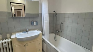 A bathroom with a sink, mirror, shower, and a brown rug on the floor.