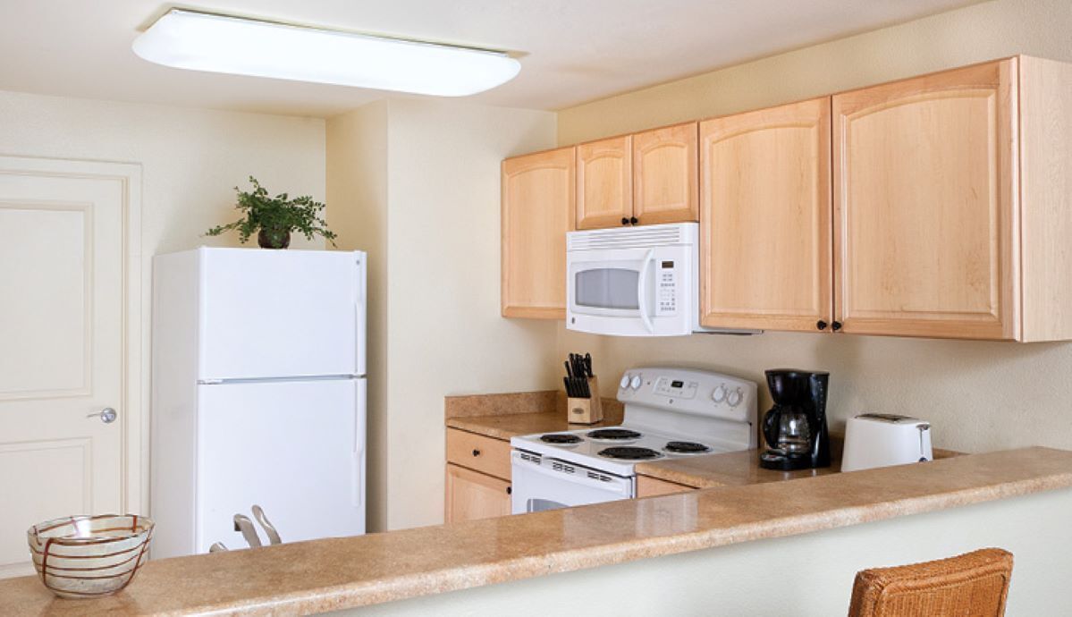 A kitchen with wooden cabinets, a white refrigerator, a microwave, a stove, and a coffee maker.