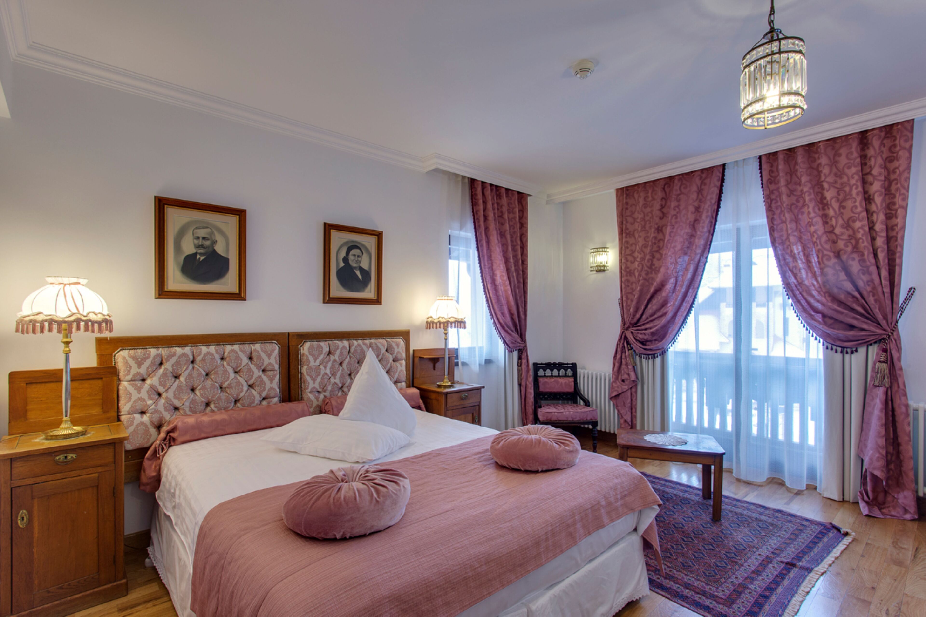 Un dormitorio con una cama grande, dos mesitas de noche, una lámpara de noche, una silla y una ventana con cortinas.
