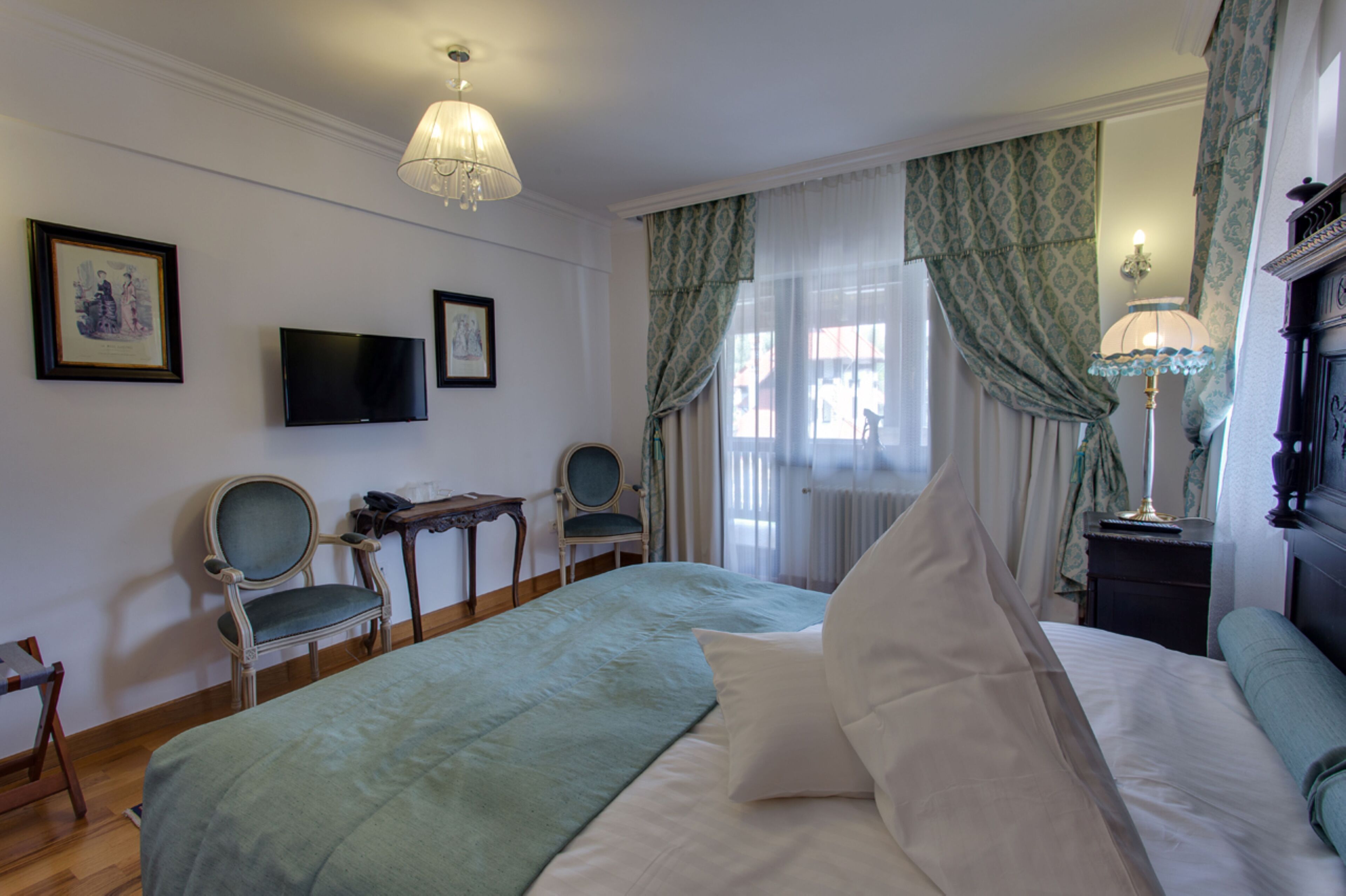 A hotel room with a bed, two chairs, a desk, a television, and a lamp.