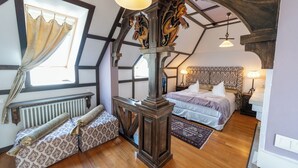 A bedroom with a large bed, a smaller sofa, a wooden headboard, and a window with curtains.