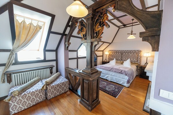 A bedroom with a large bed, a smaller sofa, a wooden headboard, and a window with curtains.