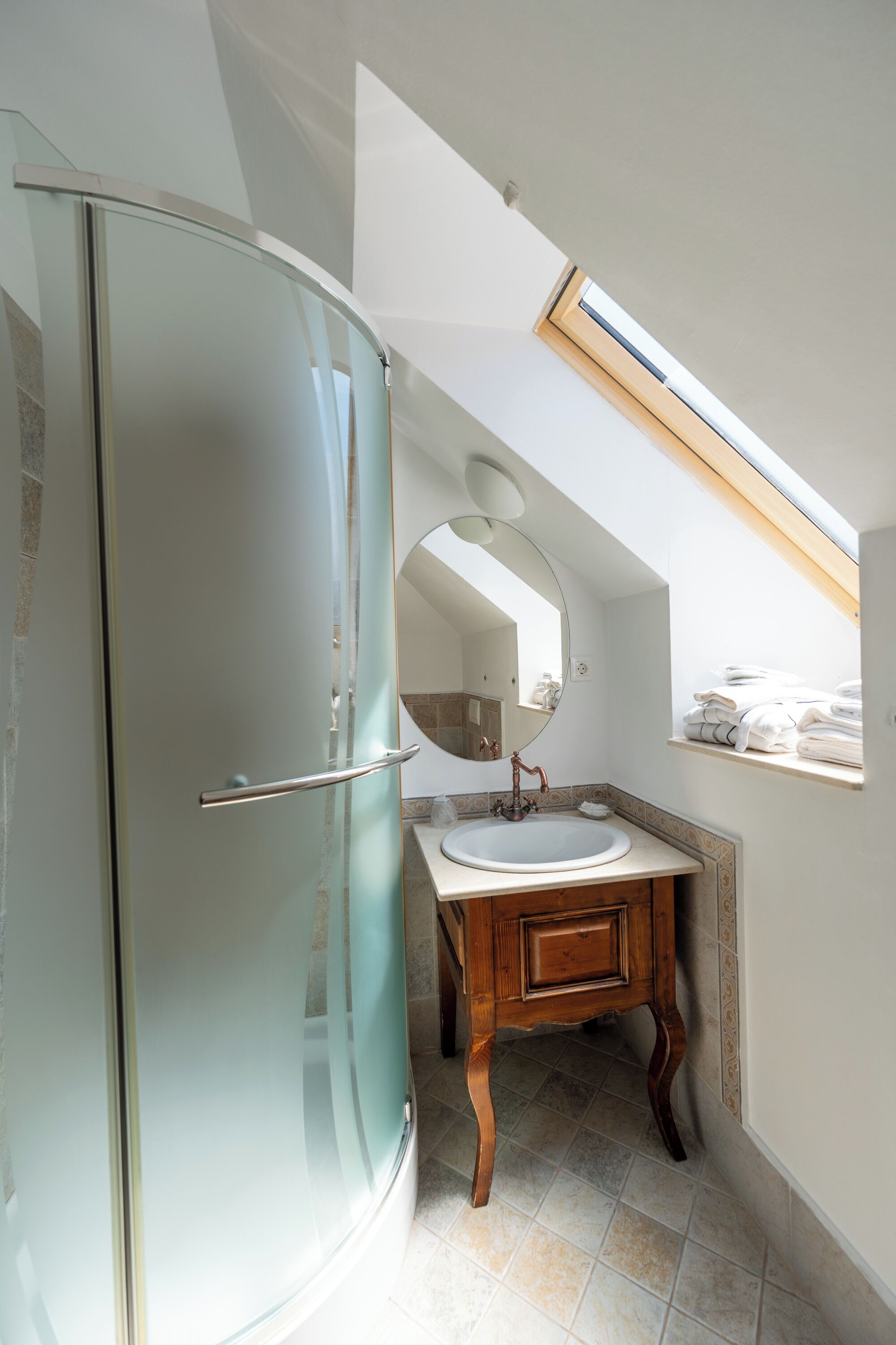 Un bagno con cabina doccia in vetro, un mobiletto vanità in legno con lavandino e un lucernario sopra lo specchio.