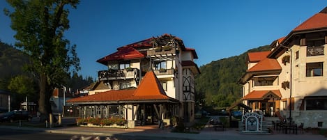 A traditional building with a red-tiled roof, a balcony, and a small outdoor seating area with tables and chairs.