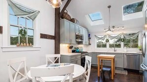 Una cocina moderna con armarios blancos, un comedor con sillas blancas y un tragaluz sobre el fregadero.