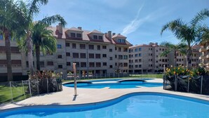 Una piscina con bordo piastrellato, circondata da palme e un edificio a più piani con balconi.