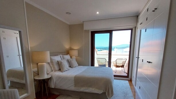 Una camera da letto con un letto grande, un tavolino, una sedia, vista sull'esterno tramite una porta scorrevole e un balcone con una poltrona.
