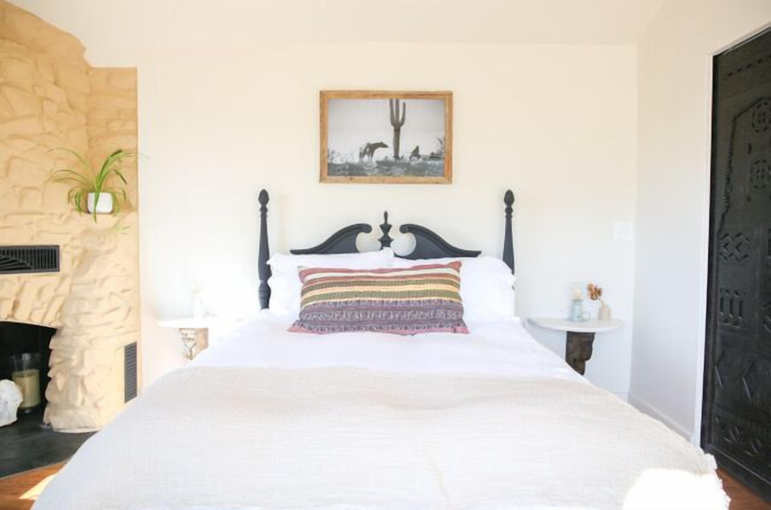 A bed with a decorative headboard, a framed picture above it, and a stone wall to the left.