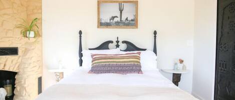 A bed with a decorative headboard, a framed picture above it, and a stone wall to the left.