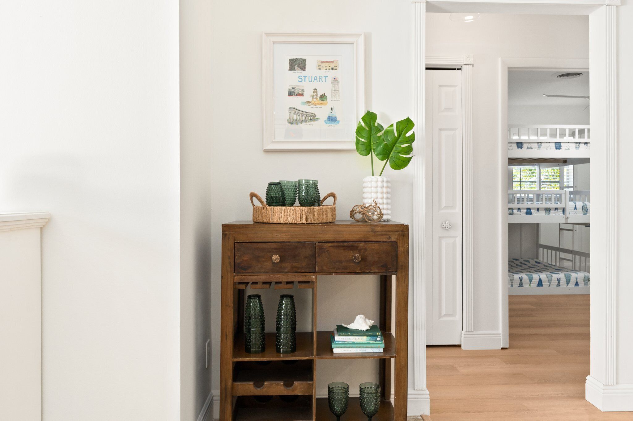 A hallway with a wooden console table, green glass vases, and a framed picture of a cityscape.