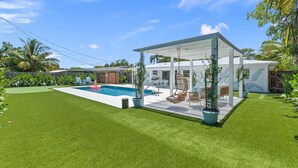 Ein Garten mit Swimmingpool, einer überdachten Terrasse und einem gepflegten Rasen.