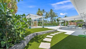 Ein gepflegter Garten mit Schwimmbad, Gartenmöbeln und einer Pergola.