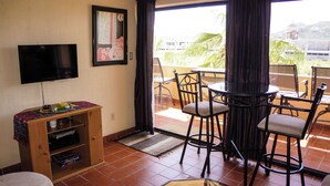 A living room with a TV, wooden cabinet, and a dining area with chairs and a table. - A-404 Enjoy Your Vacation In This Beautiful Condominium! (Cabo San Lucas)