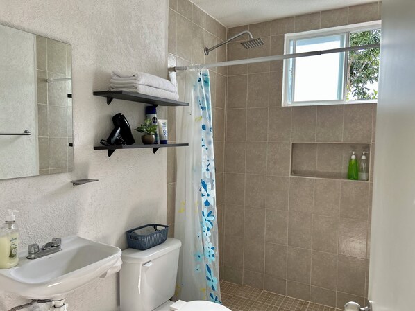 Un baño con lavamanos, inodoro, ducha y ventana con vista a árboles.