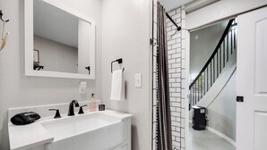 Een badkamer met een witte wastafel, een zwarte kraan en een spiegel erboven. Een handdoek hangt aan een rek en er staat een zwarte prullenbak.