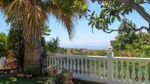 Ein Garten mit weißem Zaun, einer Palme und Blick auf eine entfernte Landschaft.