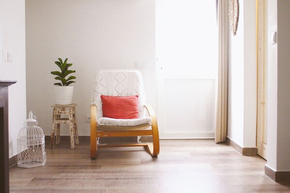 Une pièce comprenant un fauteuil à bascule en bois, une plante en pot blanche, un petit tabouret et une cage à oiseaux blanche.