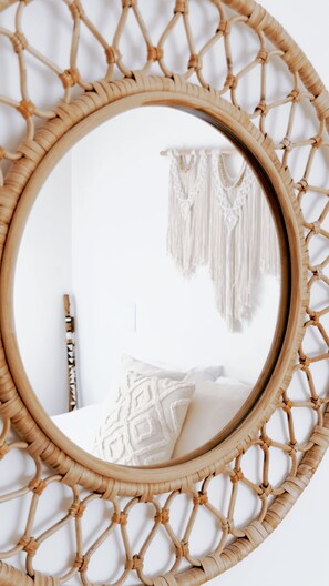 Un espejo redondo con marco tejido, una cama con almohada estampada y una pared decorada con macramé.