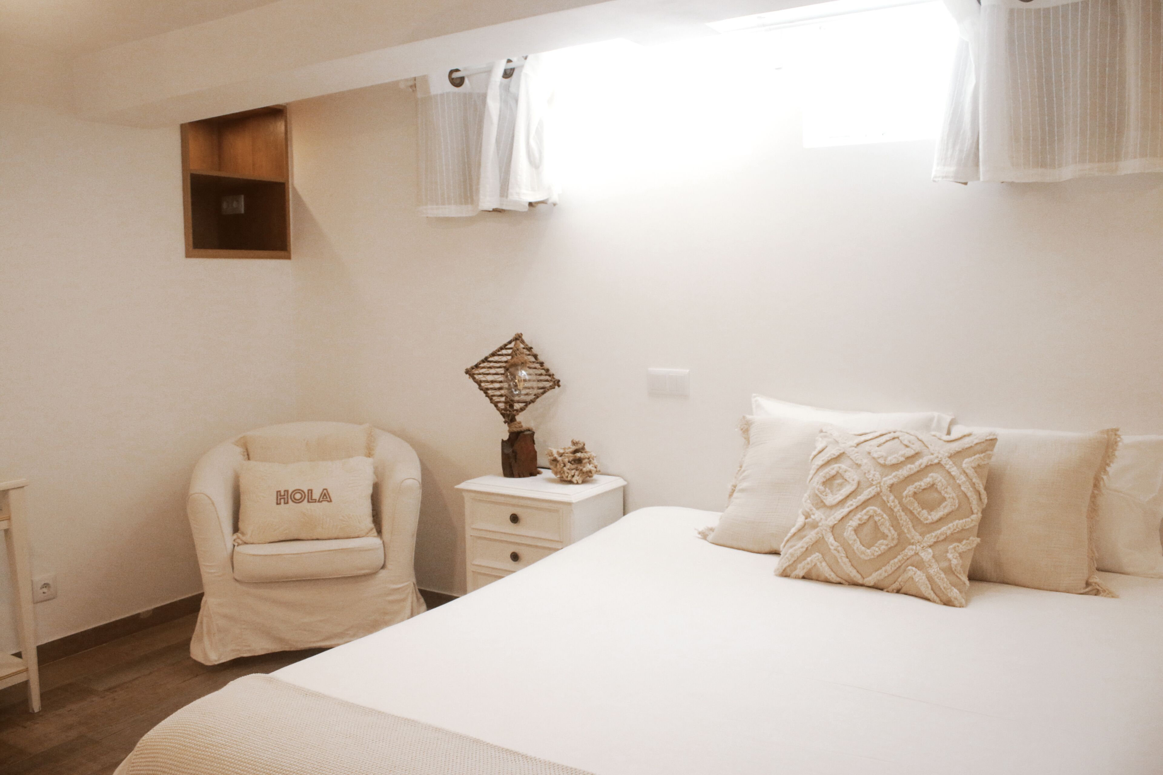 Een slaapkamer met een bed, een stoel, een nachtkastje en een klein houten plankje.