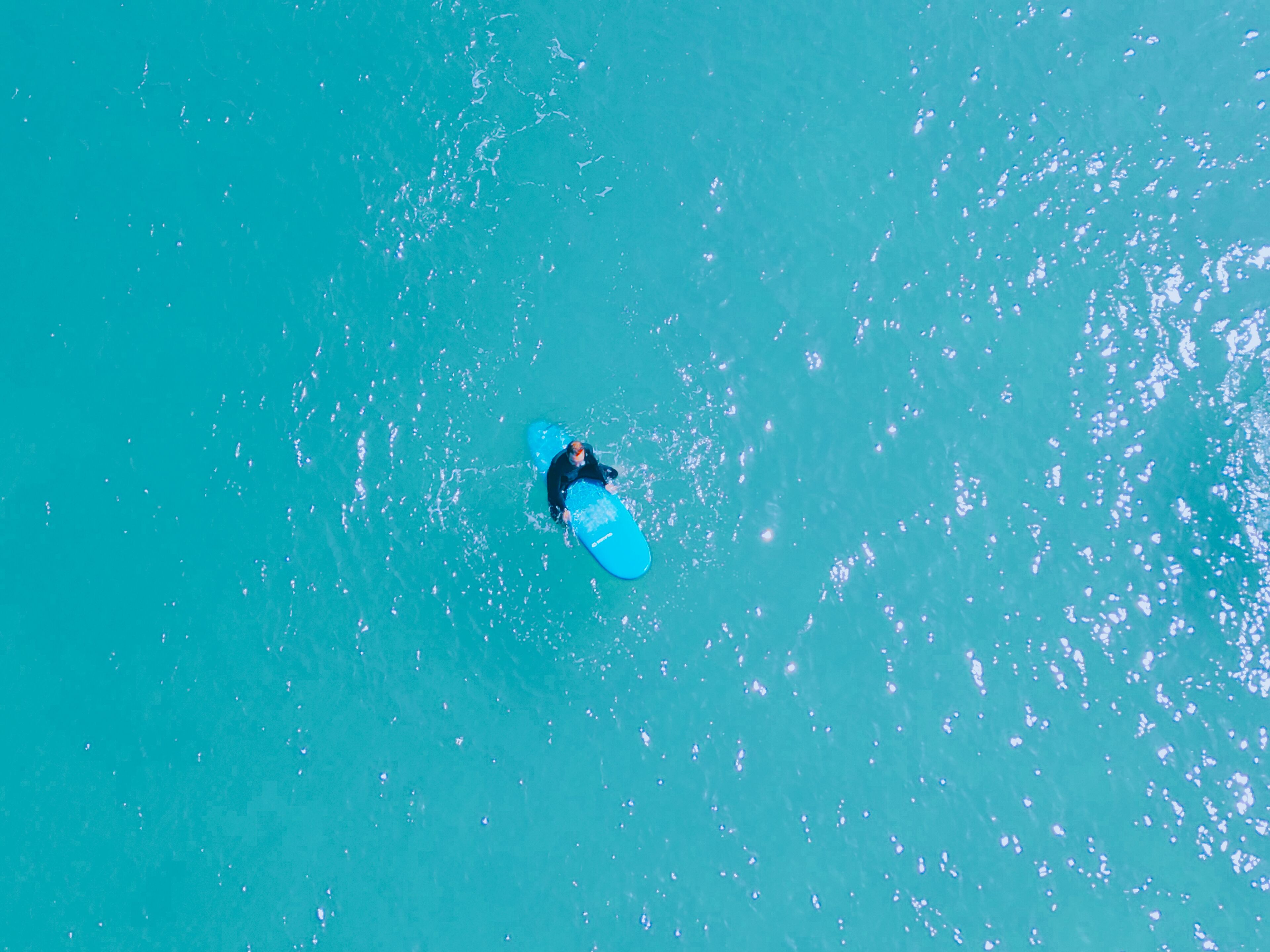 Eine Luftaufnahme einer Person, die auf einem Surfbrett in türkisblauem Wasser fährt.