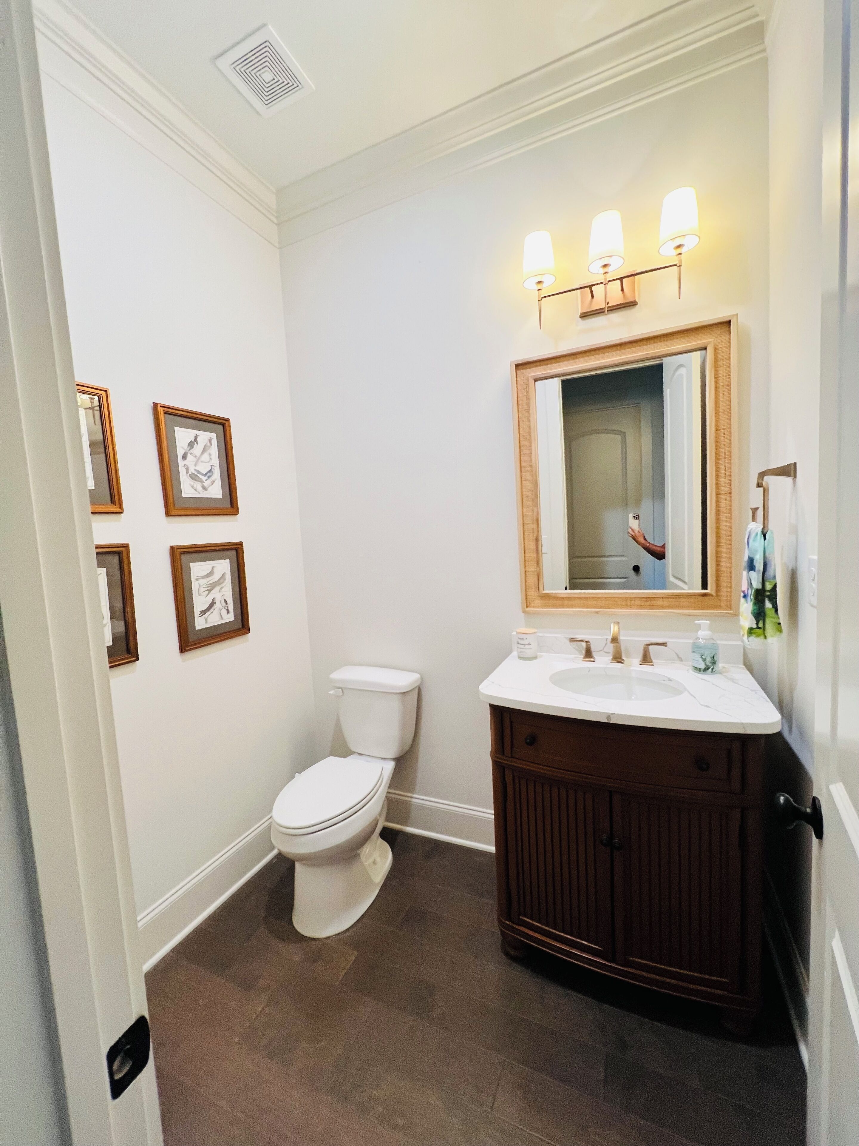 A bathroom with a toilet, sink, vanity, framed pictures on the wall, and a mirror with lights above.