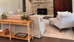 Un salon spacieux doté d’une cheminée en pierre, de poutres apparentes, d’un téléviseur fixé au mur et d’un coin salon confortable.