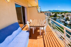 Ein Balkon mit Tisch, Stühlen und einer Couch, Blick auf eine Marina sowie Gebäude im Hintergrund.