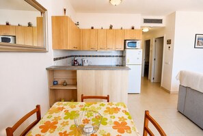 Une cuisine compacte avec des meubles en bois, un four à micro-ondes et un réfrigérateur. On y trouve une table à manger avec des chaises et une nappe à motifs floraux.