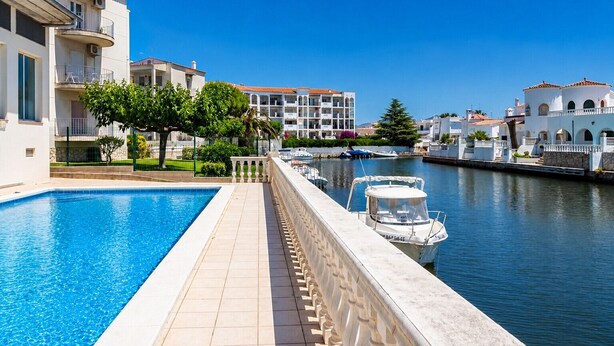 A swimming pool adjacent to a canal with boats, surrounded by white buildings with balconies. - 224-Apartment with view on marina , pool and parking (Empuriabrava)