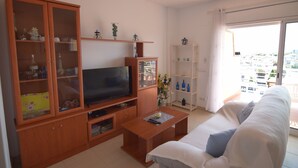 A living room with a TV, wooden cabinets, a sofa, and a balcony with a city view. - 224-Apartment with view on marina , pool and parking (Empuriabrava)