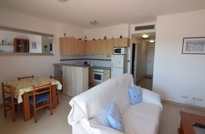 A compact living space with a kitchenette, a dining area with a table and chairs, and a white sofa with a cushion.
