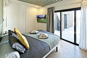 A bedroom with a bed, pillows, a television on the wall, and a view of the outside.