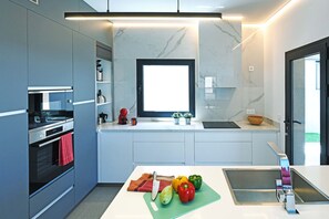 Eine moderne Küche mit integrierten Geräten, einem großen Fenster und einer zentralen Kochinsel mit Spüle und Schneidebrett.