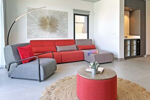 A modern living room with a grey sofa, red cushions, a grey armchair, a round coffee table with a plant, and a large abstract painting on the wall. - Salobre Las Yucas 5 (San Bartolomé de Tirajana)