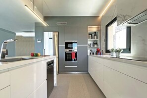 A modern kitchen with integrated appliances, a built-in oven, and a window overlooking the garden. - Salobre Las Yucas 5 (San Bartolomé de Tirajana)