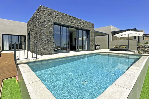 A modern house with a stone facade, a swimming pool, and a patio with outdoor furniture.
