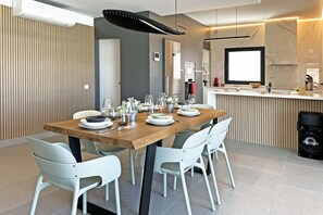Ein moderner Essbereich mit einem Holztisch, gedeckt für vier Personen, weißen Stühlen und einer Küche im Hintergrund.