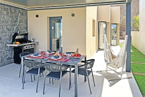 An outdoor patio with a dining table set for four, surrounded by chairs, a barbecue grill, and a hammock. - Salobre Las Yucas 5 (San Bartolomé de Tirajana)