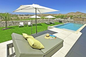 A poolside area with a green sofa, white umbrellas, and a view of a mountainous landscape. - Salobre Las Yucas 5 (San Bartolomé de Tirajana)