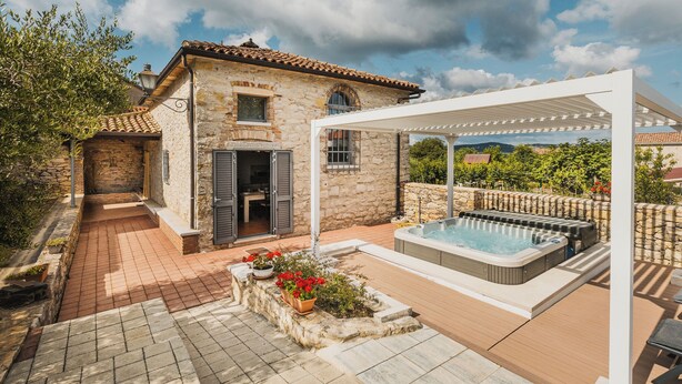 Ein Steinhaus mit Terrasse, Whirlpool und einer Pergola.