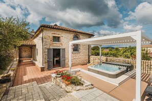 Ein Steinhaus mit Terrasse, Whirlpool und einer Pergola.