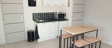 A compact kitchen with white cabinets, a black microwave, and a wooden dining table with benches.