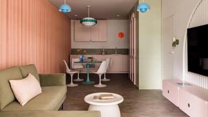 A modern living room with a sofa, a dining table with chairs, a kitchen area, and a TV on the wall. - Pops Apartment

 (Kraków)