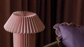 A room with a tall, ribbed, pink lamp on a white table, a purple pillow with a scalloped edge, and a dark green sofa. - Pops Apartment

 (Kraków)