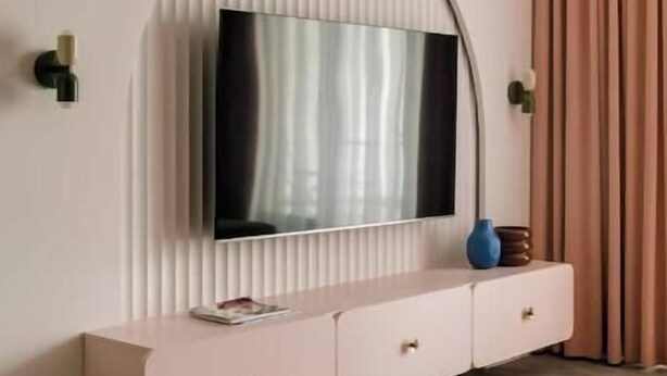 A modern living room with a large flat-screen TV mounted on a curved wall, a pink console table with drawers, and a round coffee table. - Pops Apartment

 (Kraków)