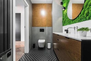 Bathroom features a unique design with a black and white polka dot floor, moss-like walls, and a mirror above the sink.